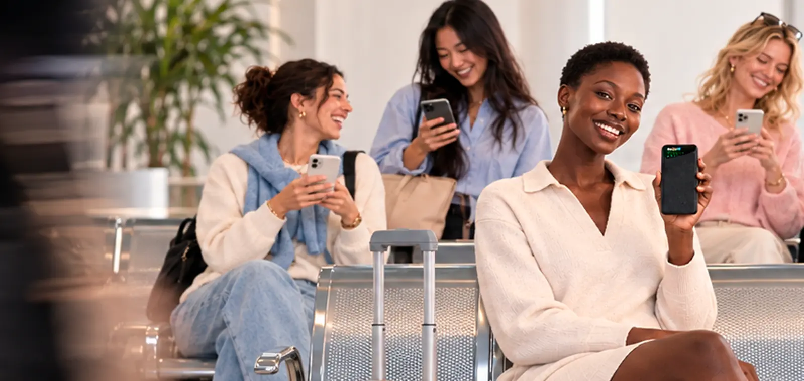 A traveler in an airport lounge holds up a Noomi pocket Wi-Fi while two friends use their phones