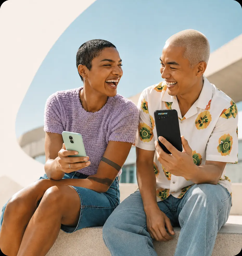 Two friends abroad laughing, one on a phone and one holding a Noomi pocket Wi-Fi